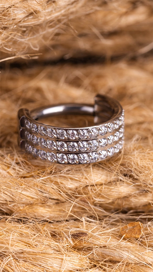 Un piercing en titane argenté posé sur un fond de paille