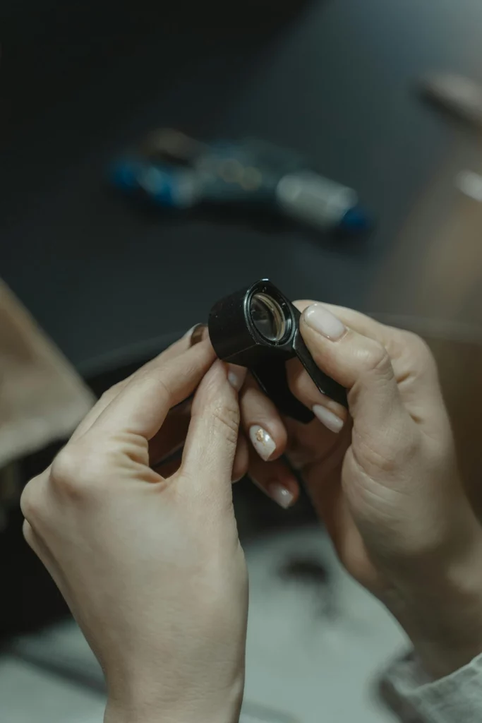 Mains inspectant un bijou de piercing à la loupe de bijoutier pour contrôle qualité
