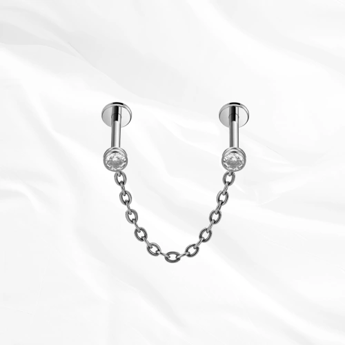Piercing en titane argenté Le Maillon, deux labrets sertis chacun d’un zircon et reliés par une chaînette en arc souple