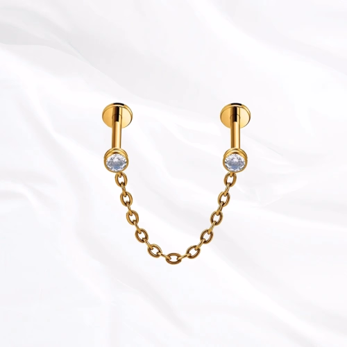 Piercing en titane doré Le Maillon, deux labrets sertis chacun d’un zircon et reliés par une chaînette en arc souple