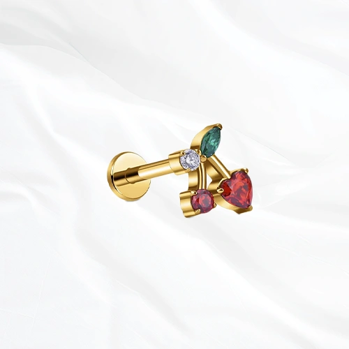 Labret en titane doré La Cerise, deux cerises rouges sur une même branche, l’une taillée en cœur et l’autre ronde, sous une feuille verte