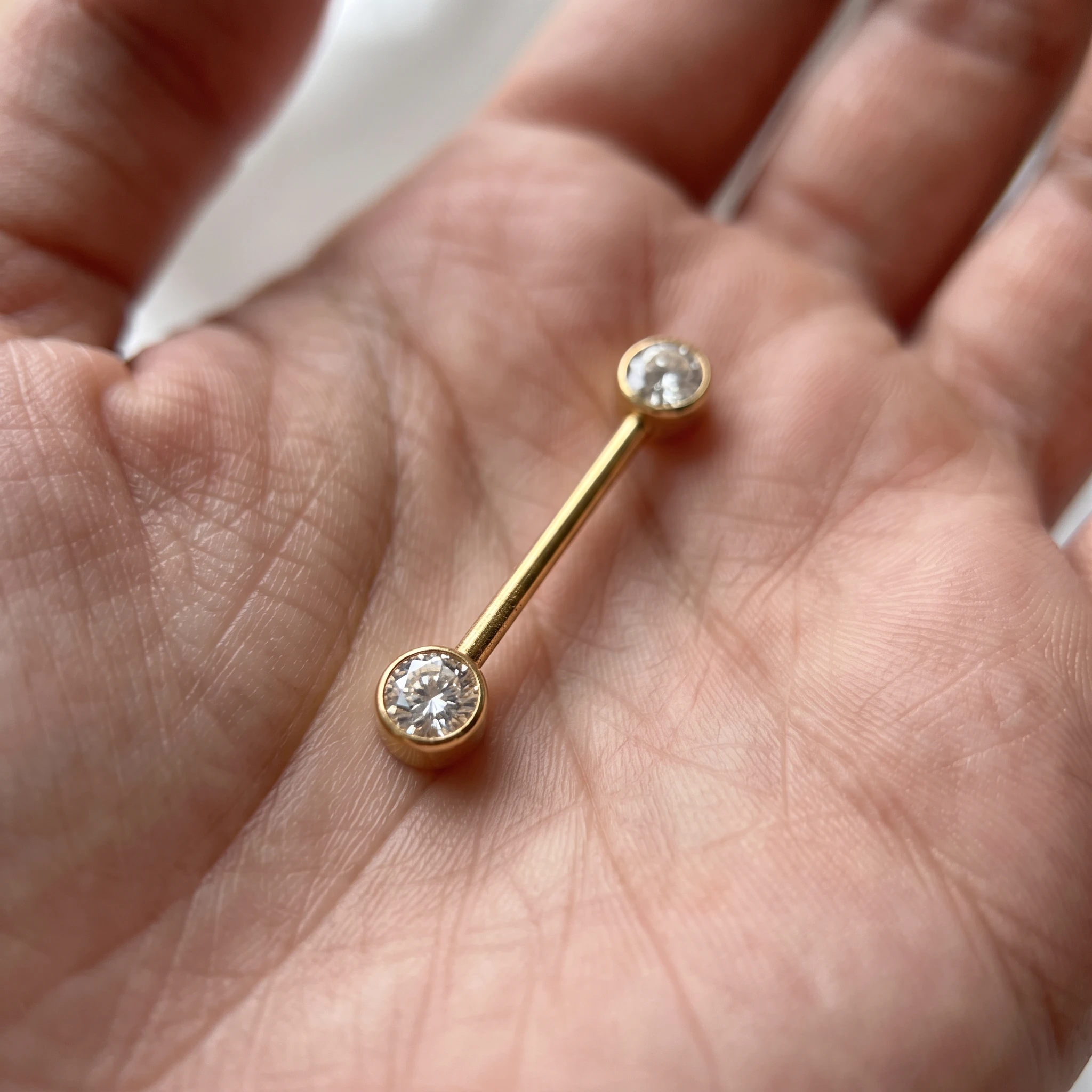 La Barre Simple Brillante en titane doré présentée au creux de la main, barre droite à deux zircons sertis clos