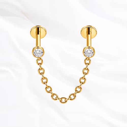 Piercing en titane doré Le Maillon, deux labrets sertis chacun d’un zircon et reliés par une chaînette en arc souple