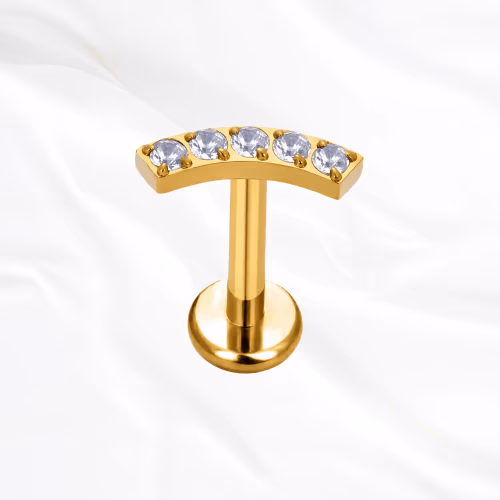 Labret en titane doré La Parabole, cinq zircons ronds alignés sur une barre légèrement arquée qui suit le relief de l’oreille
