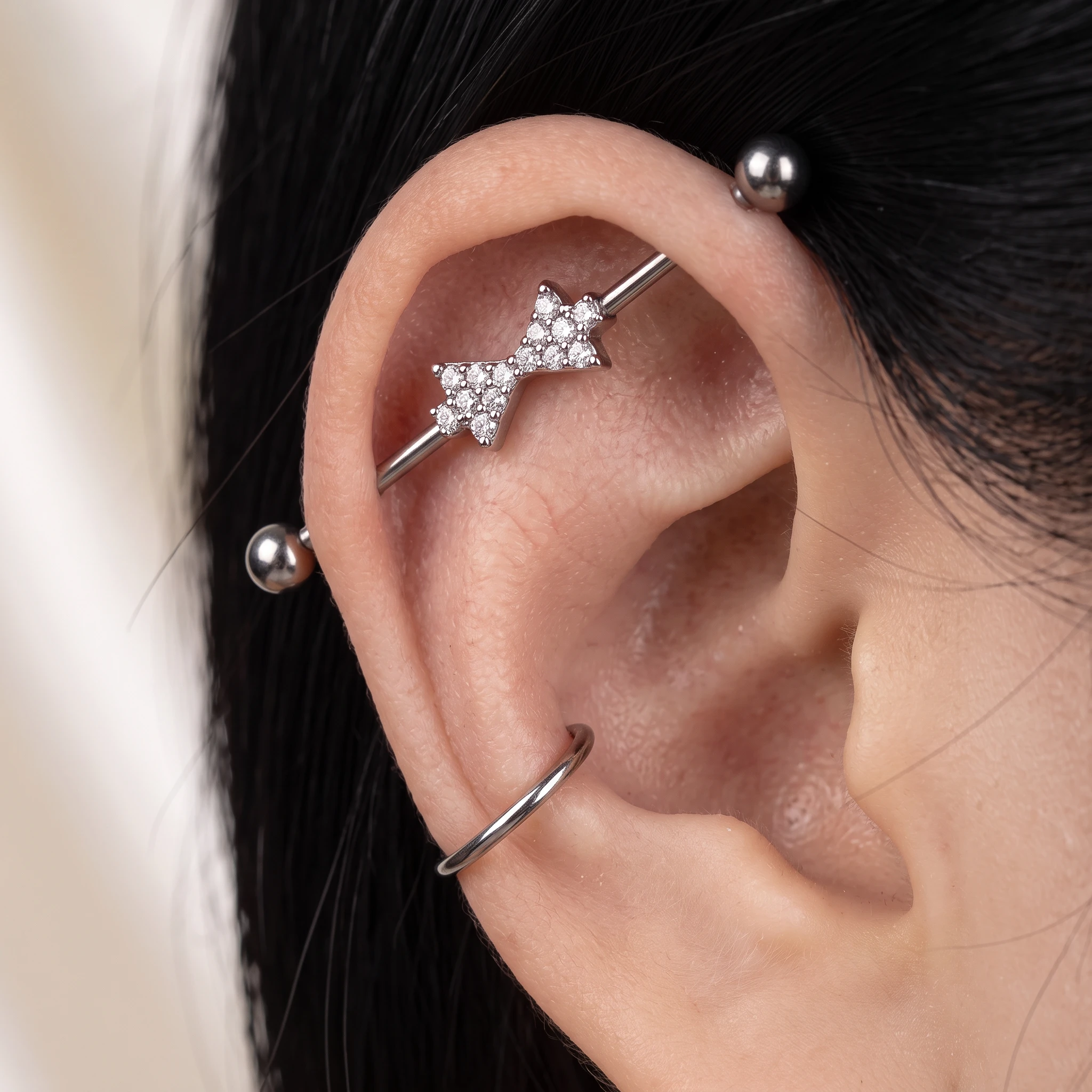 Piercing industriel en titane argenté Les Retrouvailles V3 porté, nœud papillon pavé de zircons traversant le haut de l’oreille