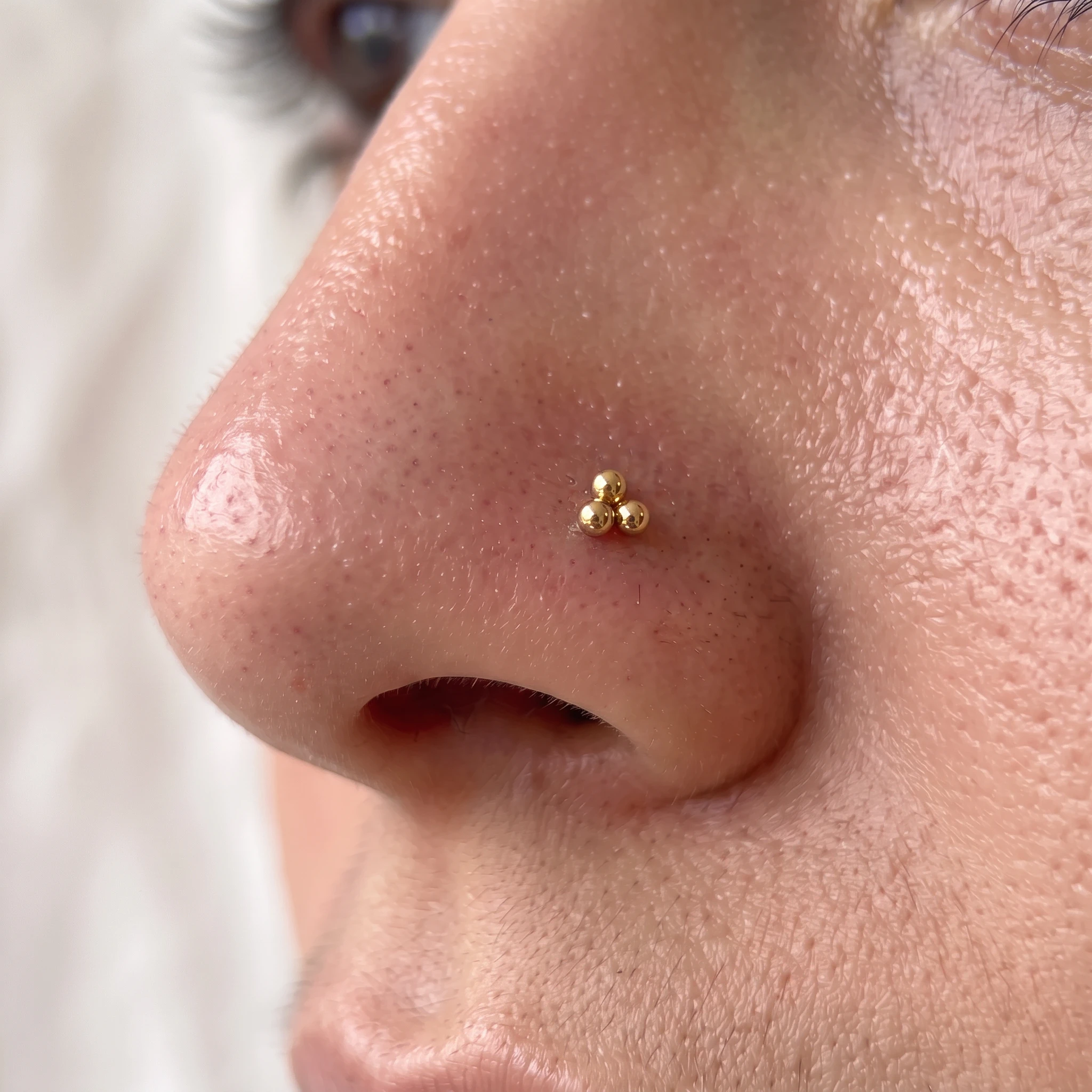 Piercing de narine en titane doré La Triforce V3 porté, trio de billes en triangle sur l'aile du nez