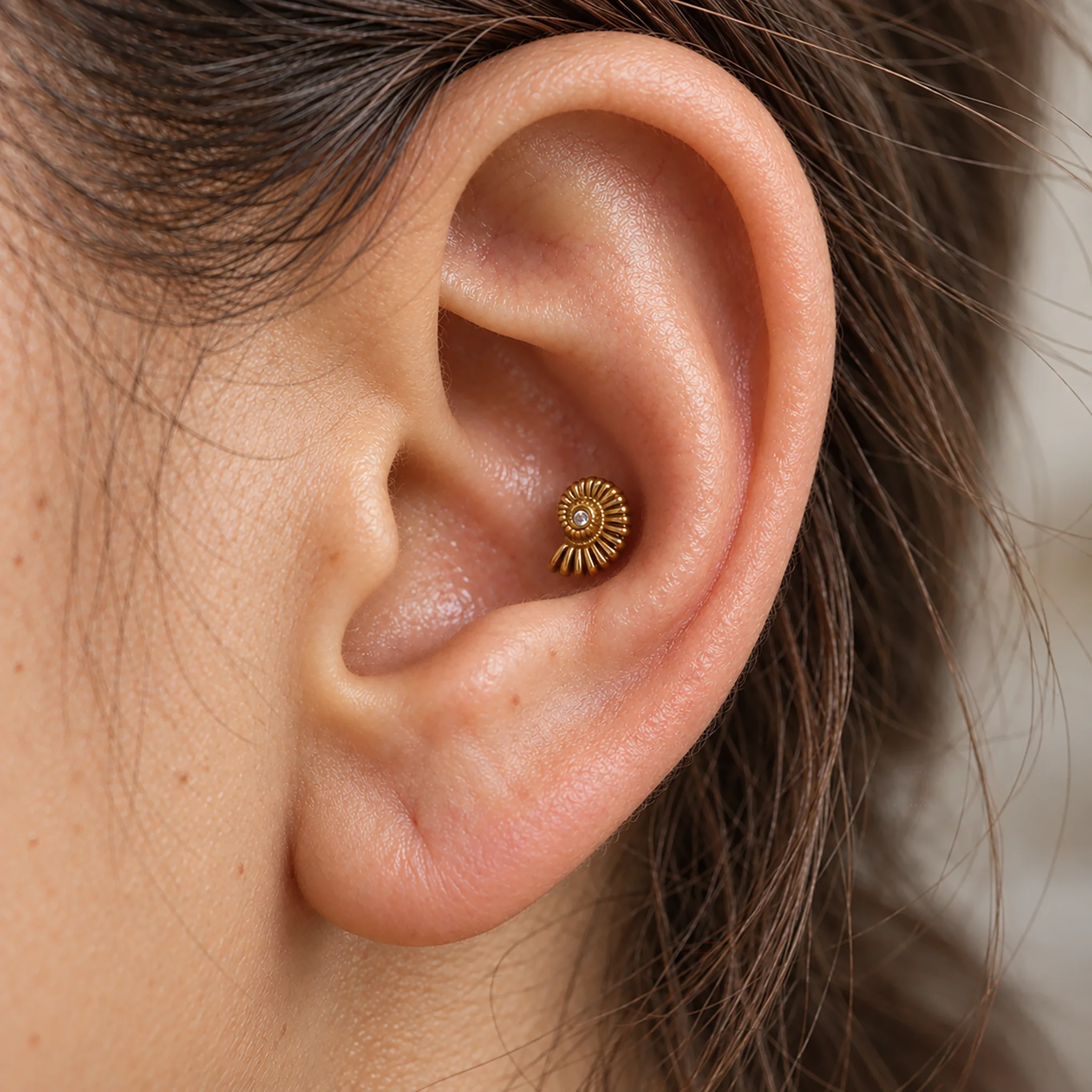 Piercing de conch en titane doré L'ammonite porté au creux de l'oreille, coquille striée et zircon central